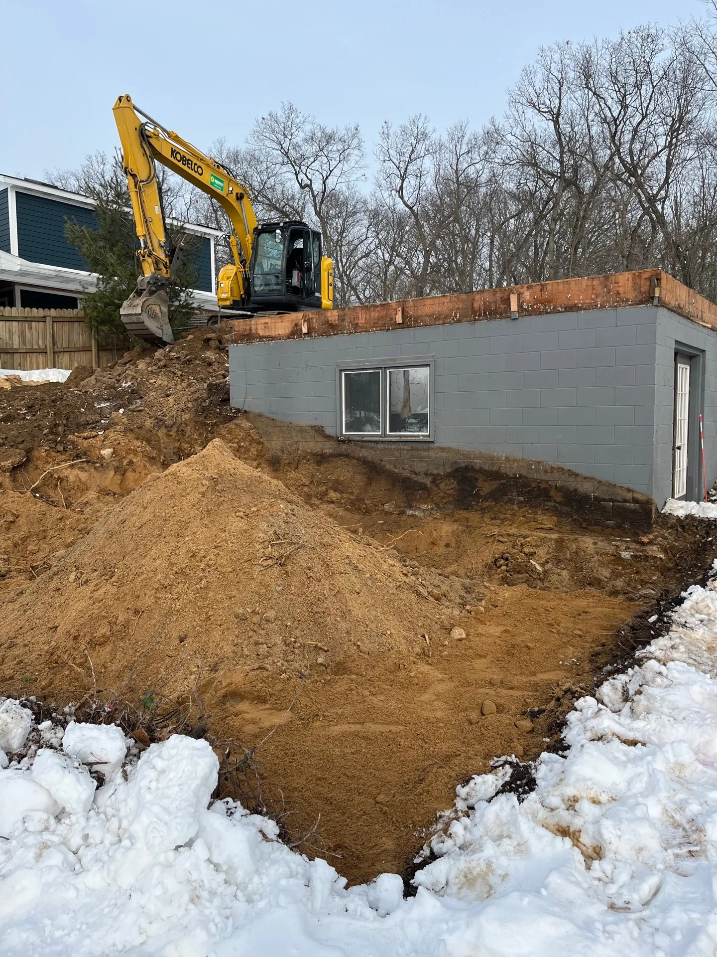 Basement foundation excavated in the snow at a Kalamazoo build site with a pile of excavated soil