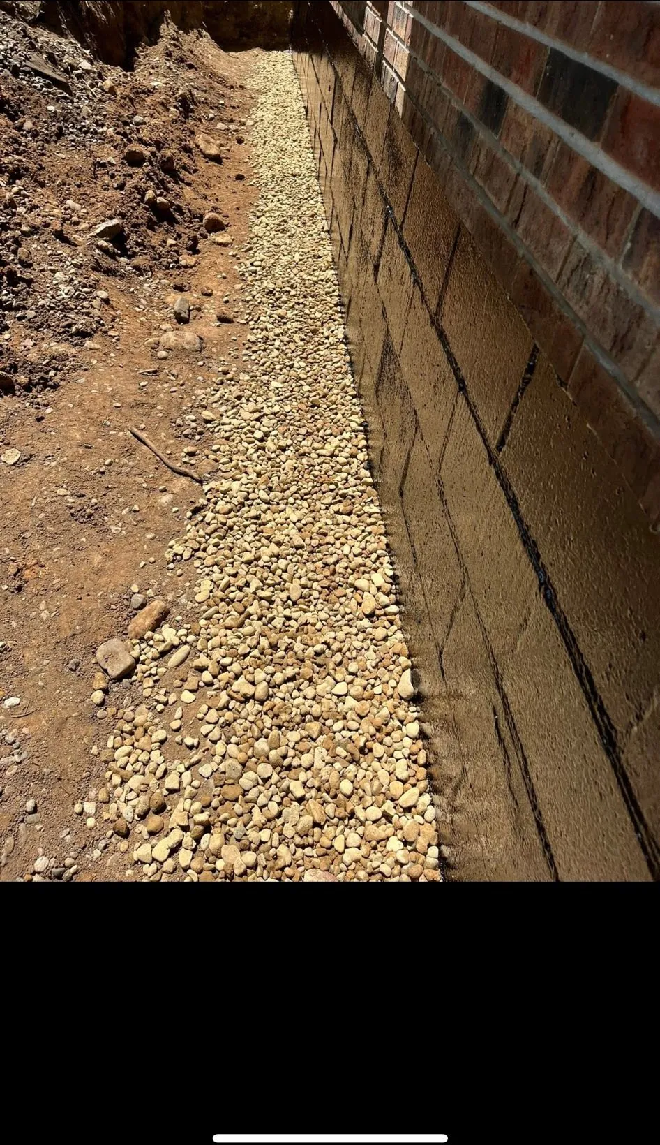 Drainage stone backfilled against a waterproofed block foundation wall